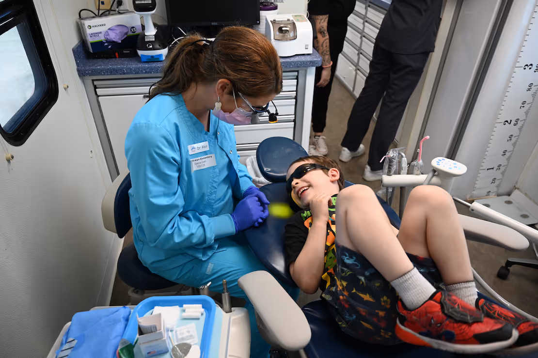 A young boy sitting in a dental chair being examined by a doctor.