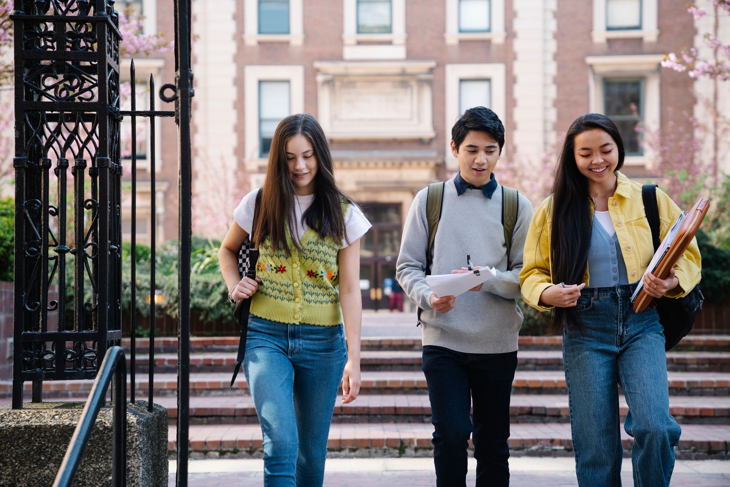 Three students walking down the steps of a brick campus building with papers and notebooks
