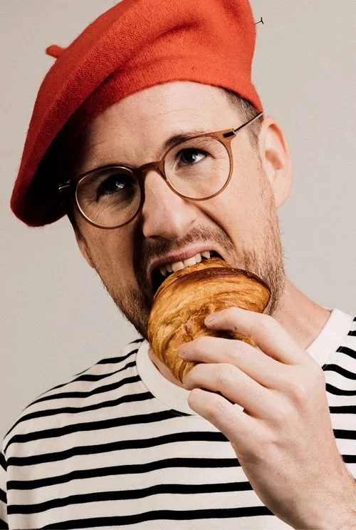 Portrait of Paul Taylor with a beret eating croissant