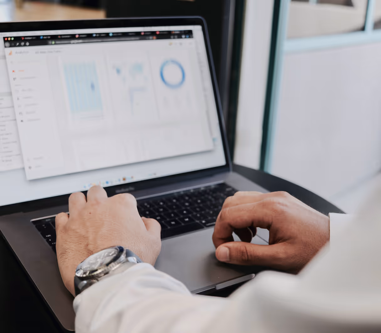 A person in a white shirt is working on a laptop displaying data analytics, with graphs and charts. The mood is professional and focused.