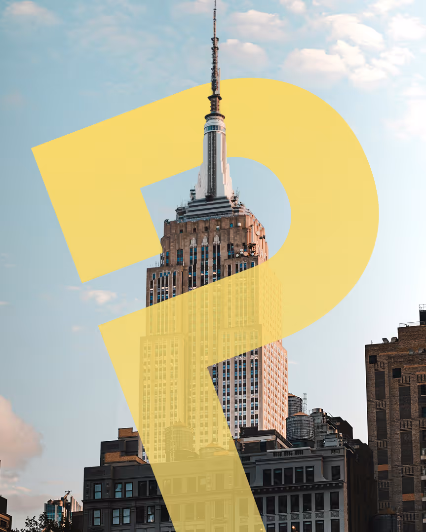 Tall iconic skyscraper with a spire, against a backdrop of blue sky and clouds, surrounded by shorter buildings. Calm urban environment.