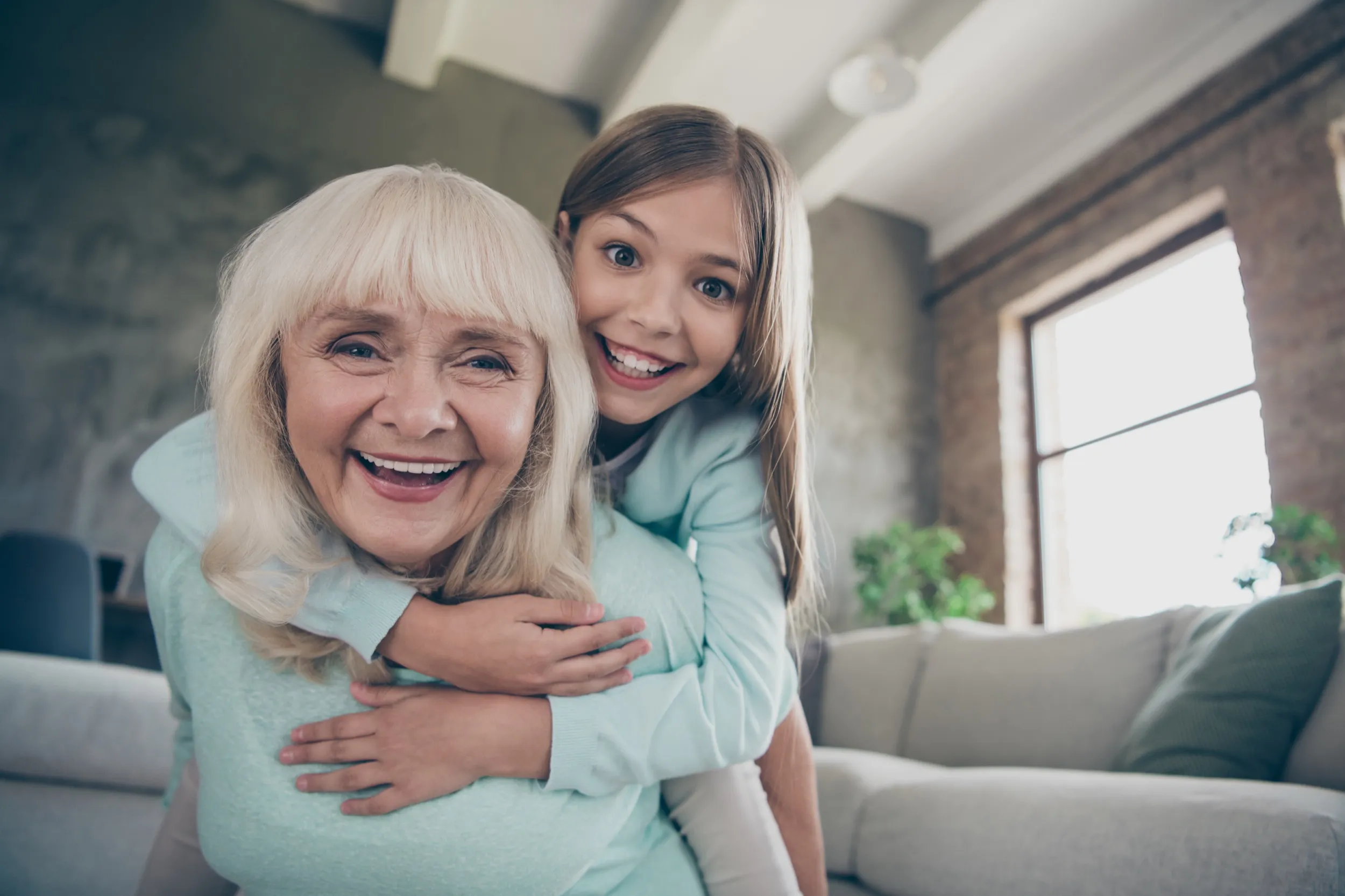 Smiling elderly woman giving a piggyback ride to a joyful young girl in a cozy living room.