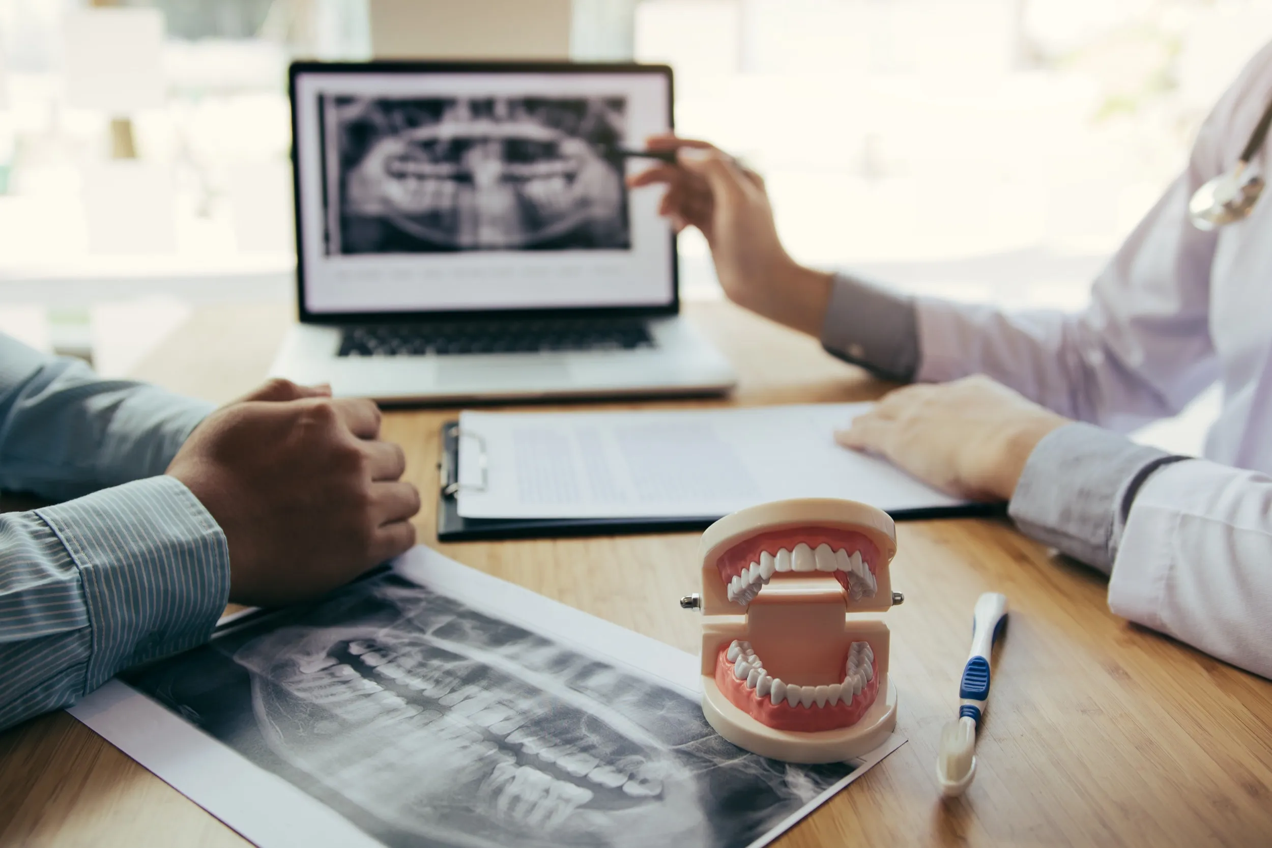 Dental consultation with X-rays, teeth model, and laptop on desk