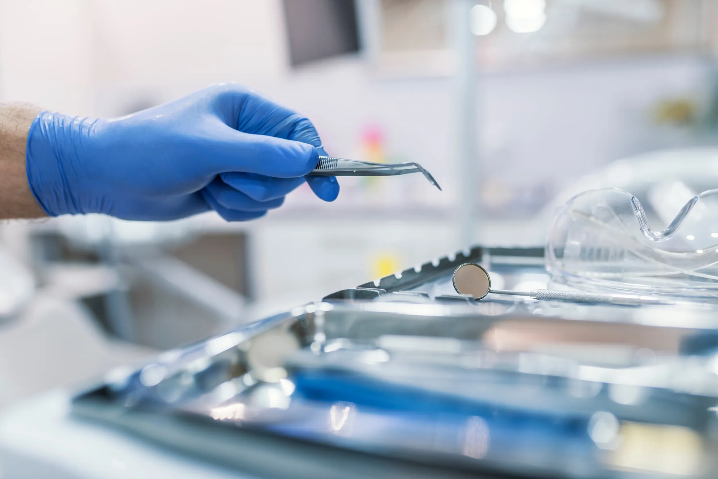Blue gloved hand holding dental tool near surgical instruments tray