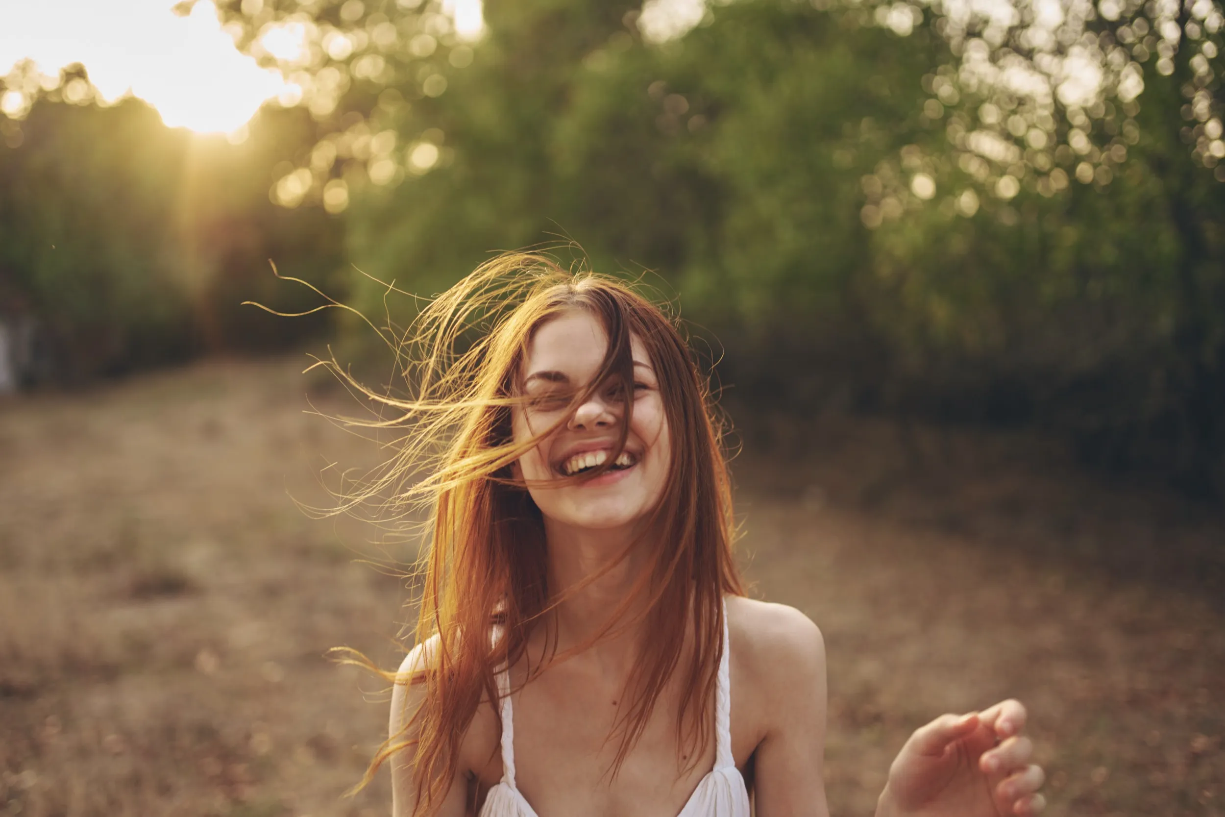 Joyful woman with windswept hair laughing in golden sunlight outdoors
