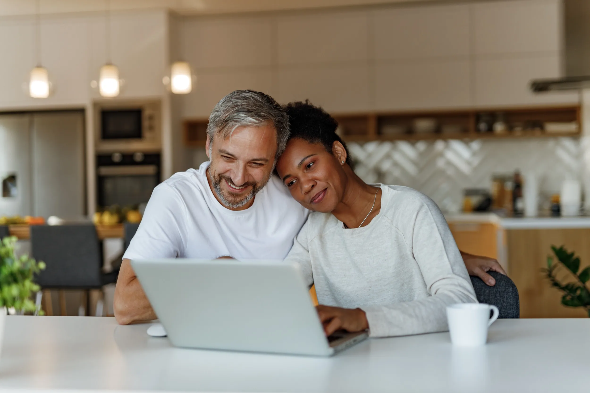 Couple smiling together while using laptop in modern kitchen