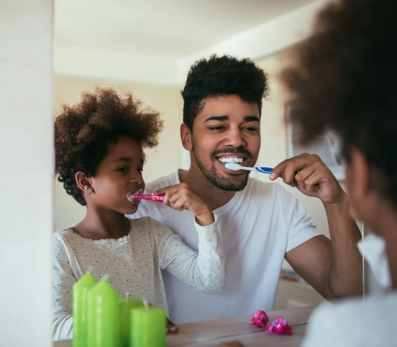 Parent and child brushing teeth together in bathroom mirror