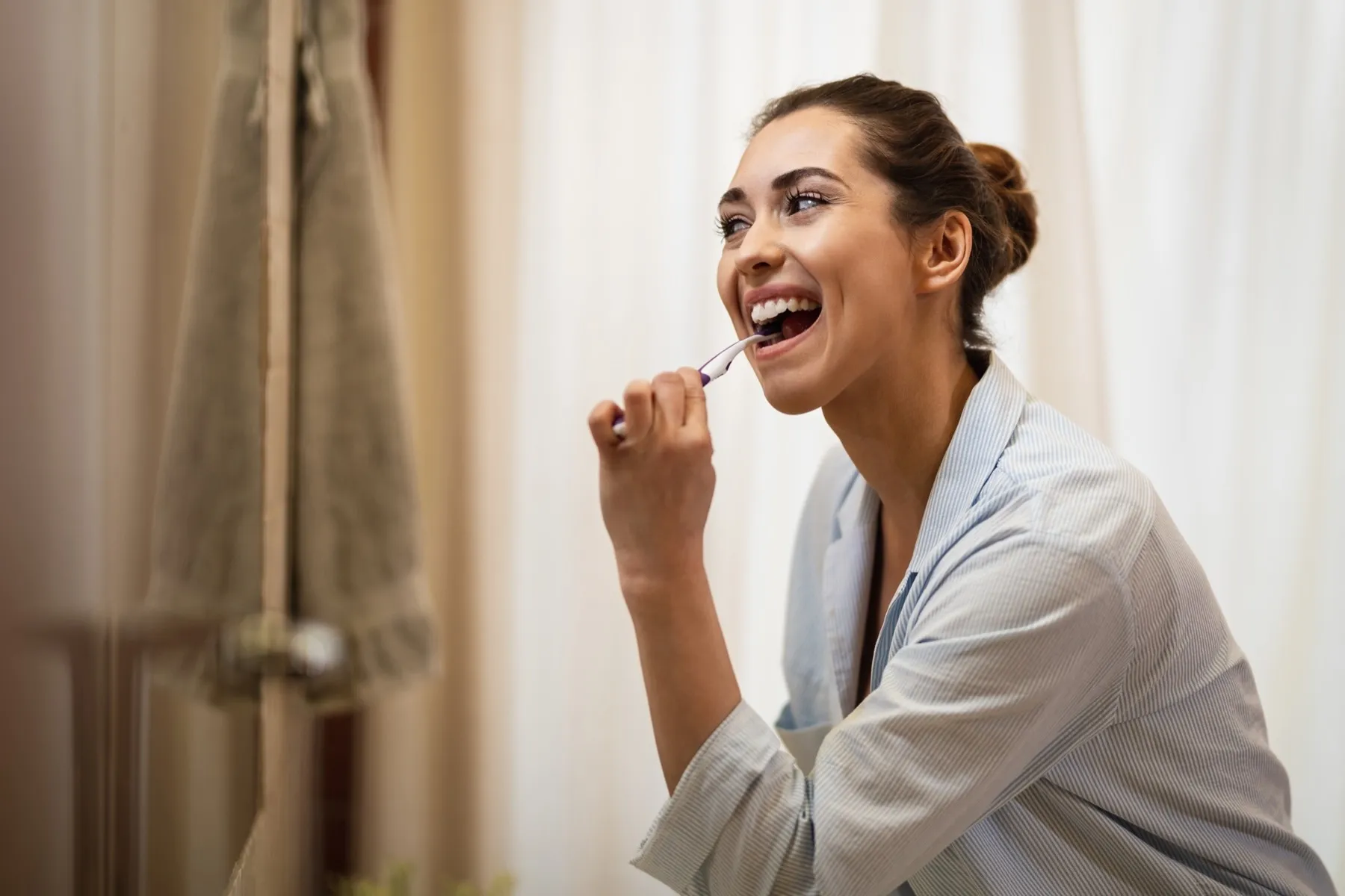 Woman in bathrobe brushing teeth and laughing joyfully at home