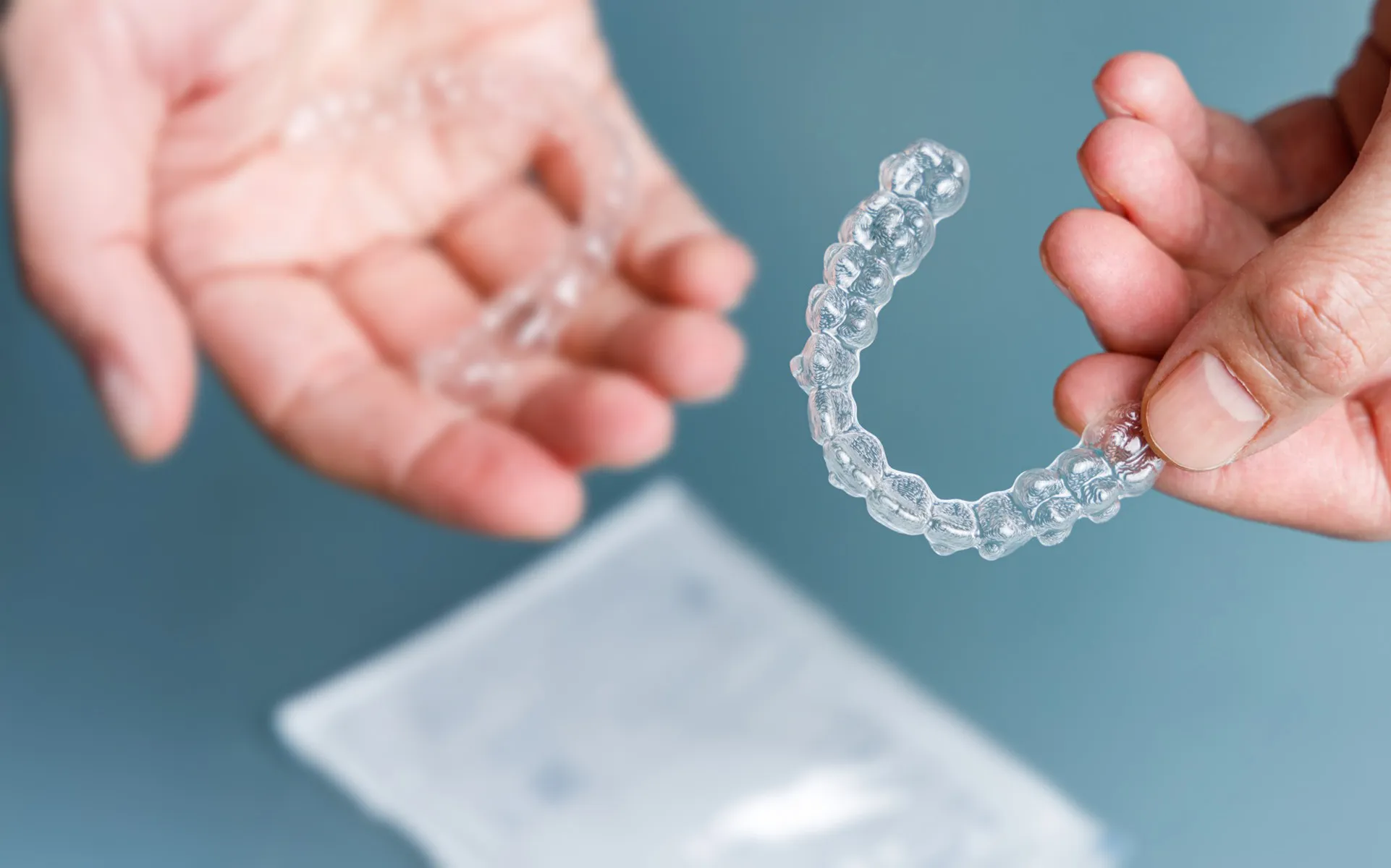 Transparent dental aligners held between two hands against blue background