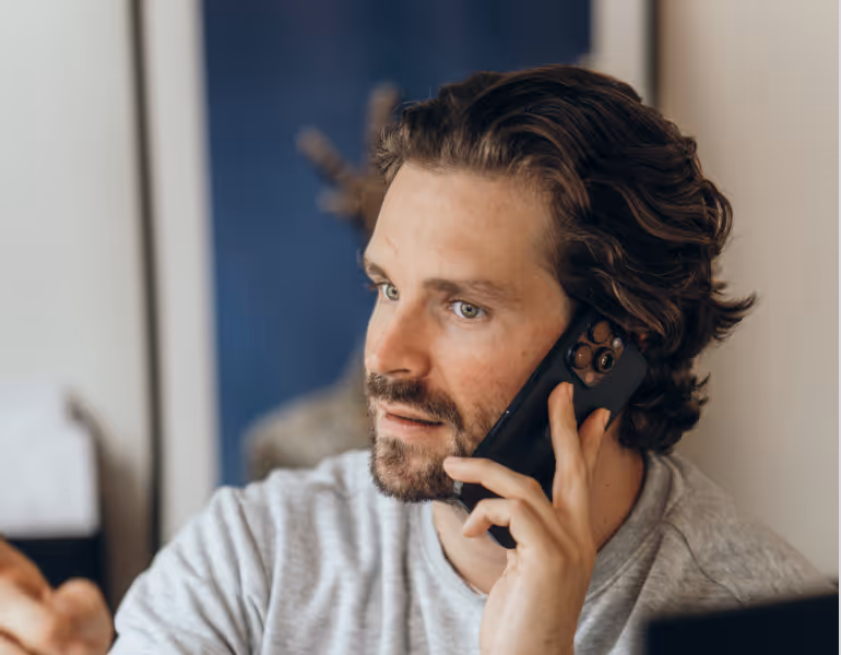 Mann mit braunen, lockigen Haaren spricht am Smartphone und blickt nach links.