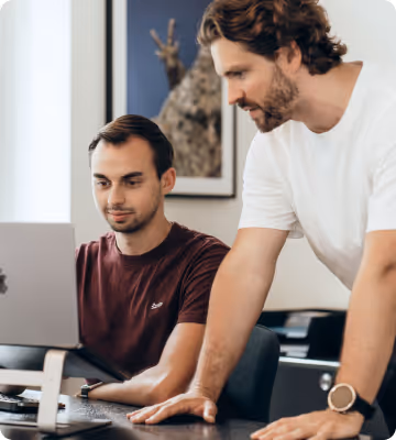 Zwei Männer arbeiten gemeinsam an einem Laptop in einem Büro mit moderner Einrichtung.