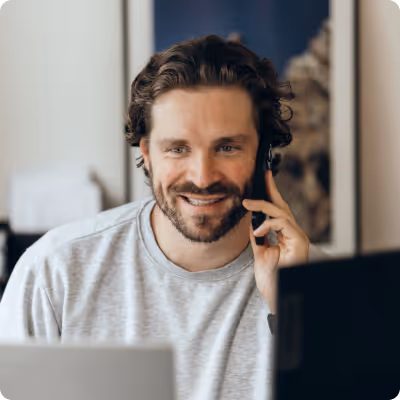 Mann mit Locken und Bart, der am Computer arbeitet und mit Headset telefoniert.
