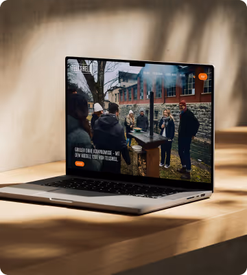 Laptop zeigt eine Webseite mit einer Gruppe von Menschen, die draußen an einem Holztisch vor einem Gebäude stehen.