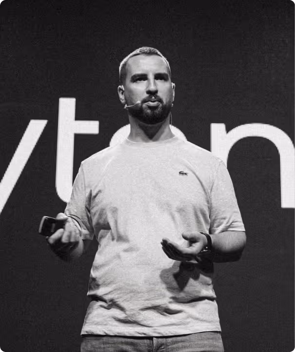 Ein Mann mit Mikrofon spricht vor großem Bildschirm mit teilweise sichtbarem Text.