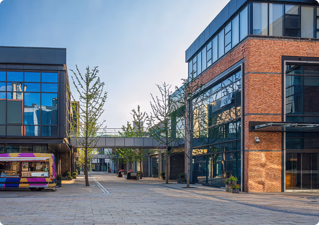 Moderne Geschäftsgebäude mit Glasfassaden, Bäumen und einem bunten Imbisswagen an einem sonnigen Tag.