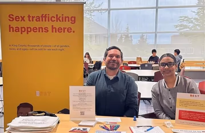 Two representatives sitting at an informational booth for REST, an organization raising awareness about sex trafficking prevention in King County.