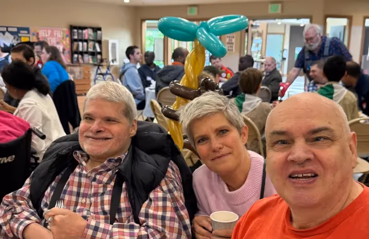 People socializing and smiling at a community event, with balloons and decorations in the background.
