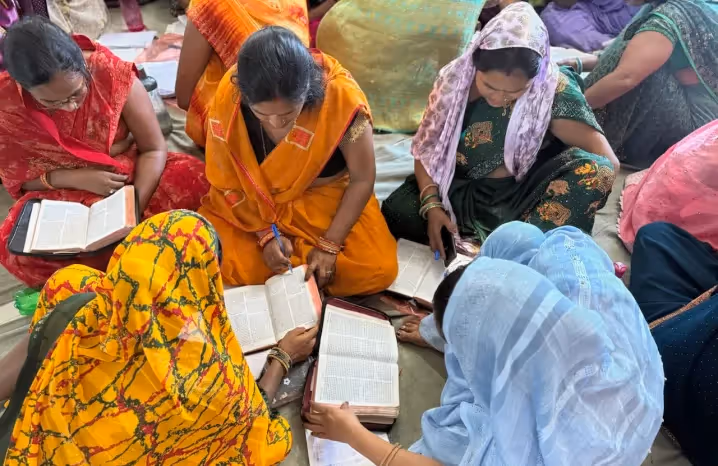 Women dressed in colorful saris sitting together and reading Bibles during a study session.