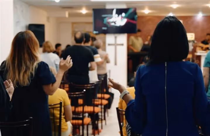 Congregation standing and worshipping in a church service, with a cross and worship lyrics displayed on a screen.