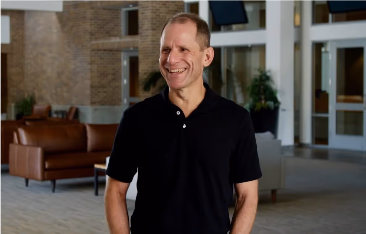 Smiling middle-aged man in black polo shirt standing in modern office.