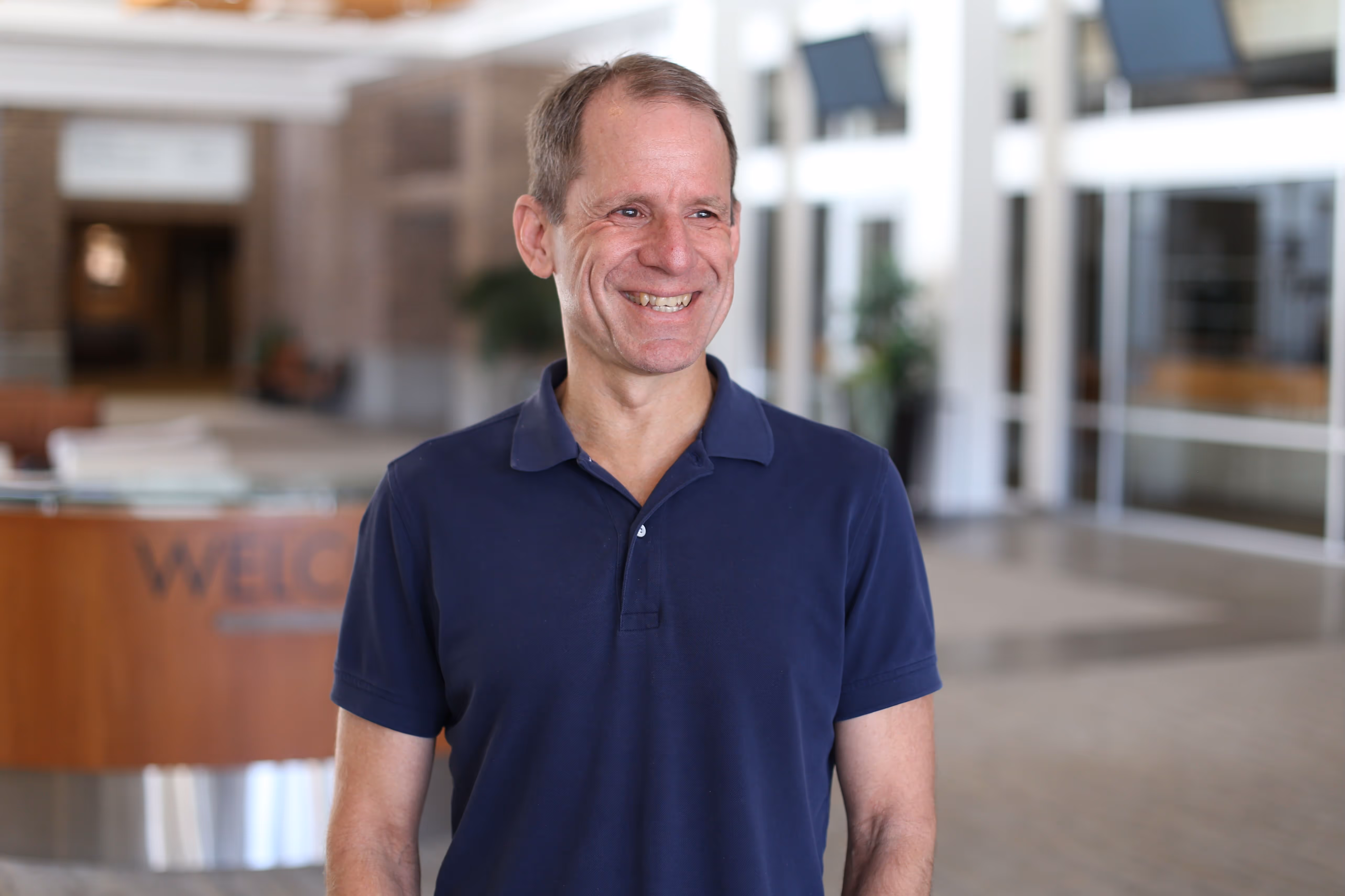 Smiling middle-aged man in black polo shirt standing in modern office.