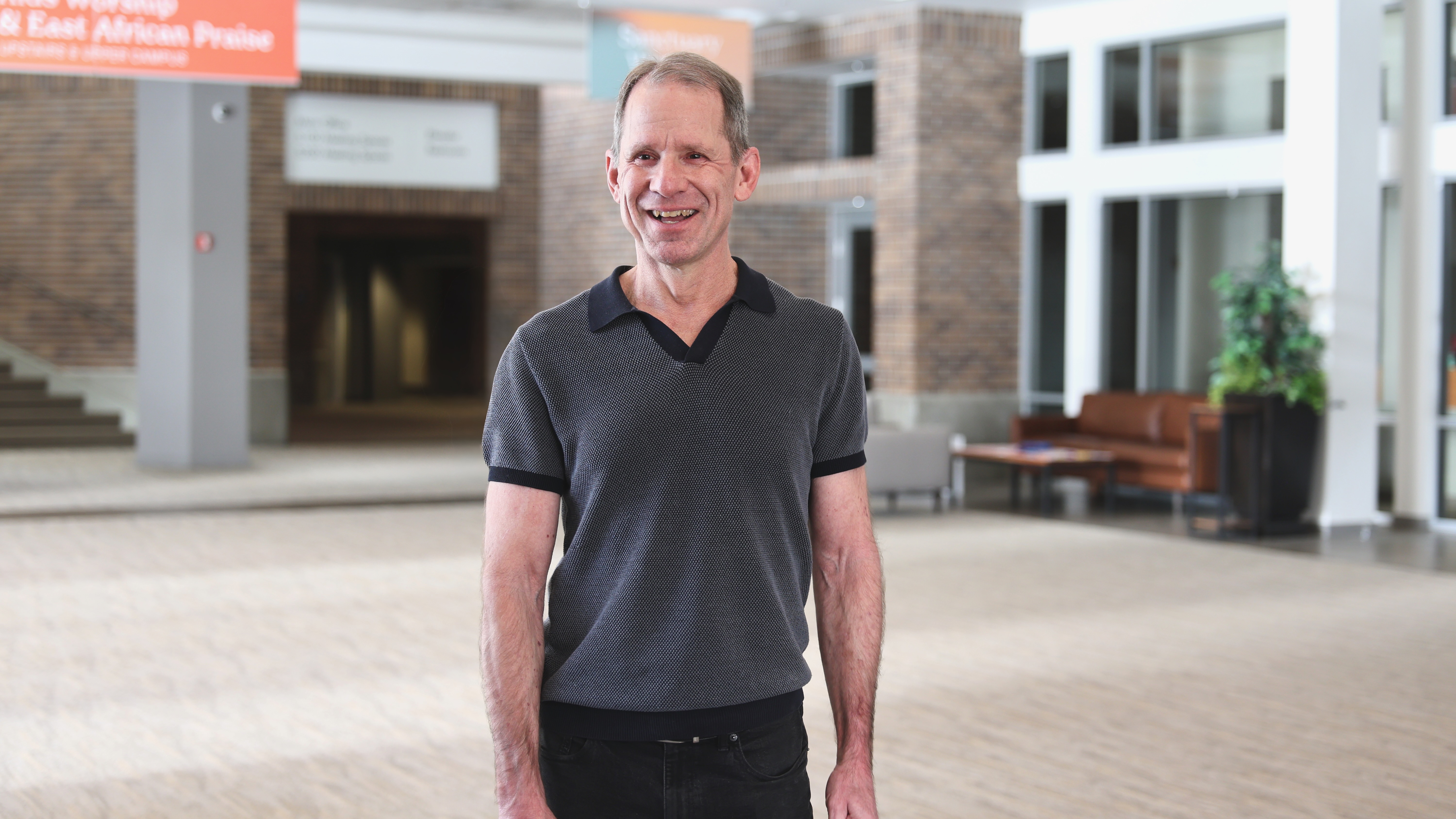 Smiling middle-aged man in black polo shirt standing in modern office.