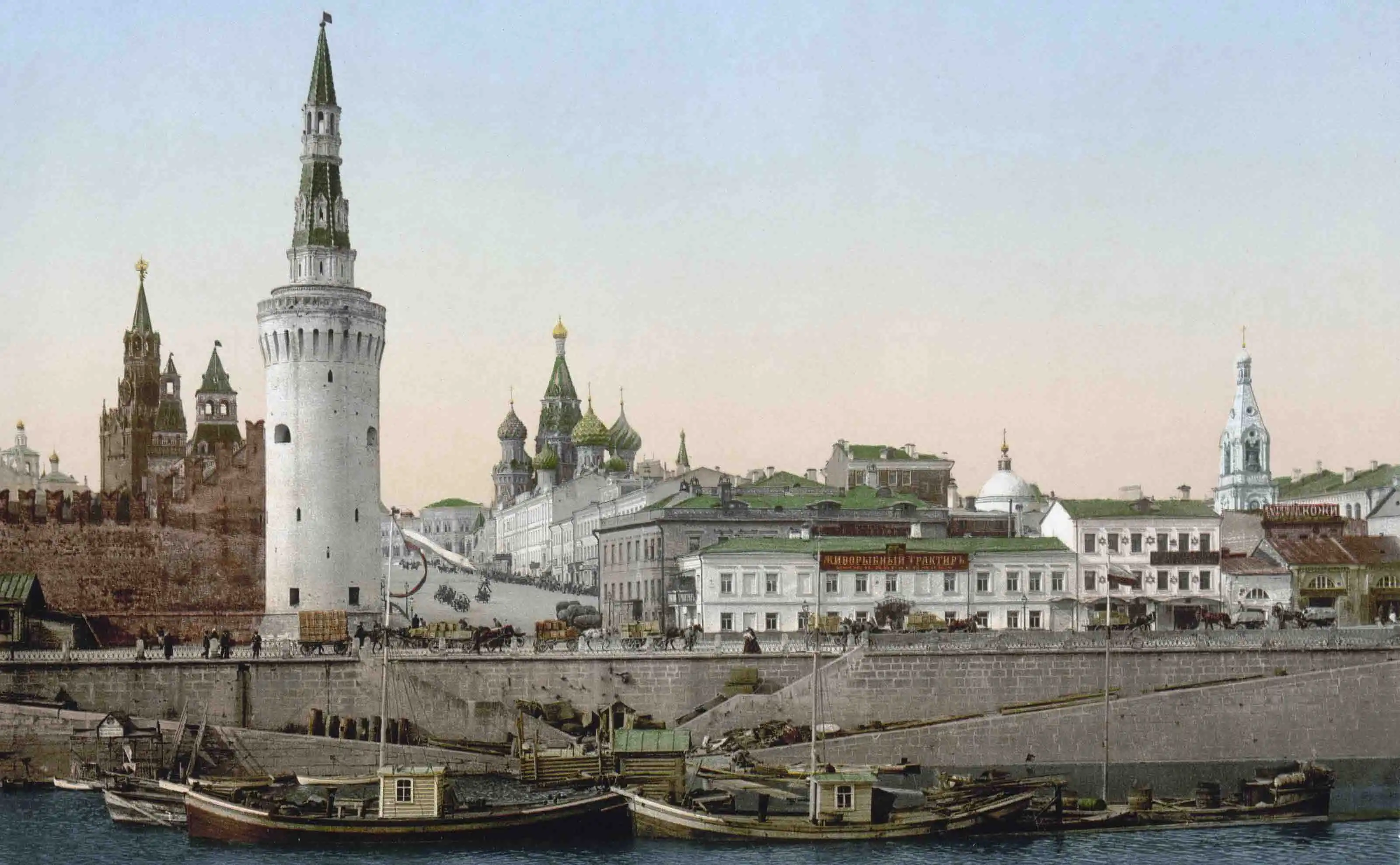 Imagem litográfica colorida histórica do rio Moscou e do Kremlin de Moscou do final do século XIX. A margem é feita de grandes blocos de pedra cinza, com barcos de carga de madeira atracados. Sobre uma elevação junto à água, ergue-se a circular Torre Vodovzvodnaya e estendem-se as muralhas da fortaleza, que estão completamente cobertas por cal branca, contrastando com a sua aparência vermelha moderna. Ao fundo, atrás das muralhas, avistam-se as cúpulas verdes da Catedral da Intercessão da Santíssima Mãe de Deus sobre o Fosso e torres do centro histórico sob um céu claro.