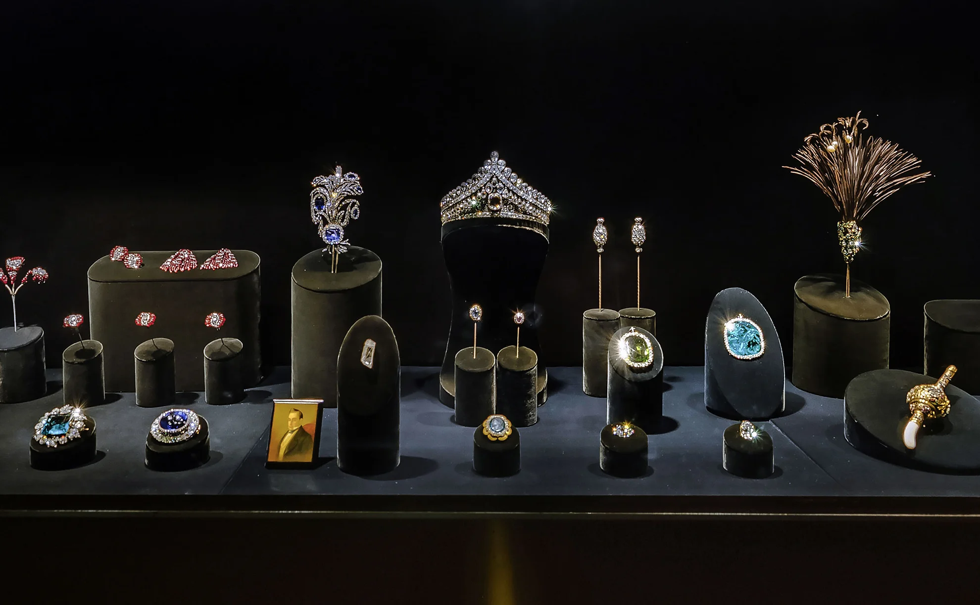Regalias de Estado dos monarcas russos na exposição do Fundo de Diamantes sobre mantos de arminho e tecidos dourados com brasões bordados. Ao centro, destaca-se a Grande Coroa Imperial em estrutura rendada de prata incrustada de diamantes, ladeada por duas fileiras de pérolas e encimada por um espinélio vermelho-escuro com cruz. À esquerda repousa a Pequena Coroa Imperial, em diagonal apoia-se o cetro de ouro com o diamante Orlov, à direita surge a orbe de ouro coroada por uma safira azul, e em primeiro plano exibe-se o colar e a estrela de brilhantes da Ordem de Santo André.