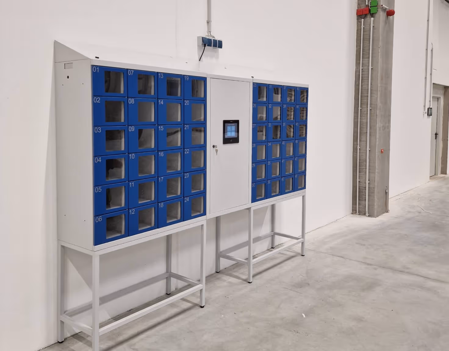 Wall-mounted white and blue locker system with numbered compartments and a central control panel in a spacious industrial room.