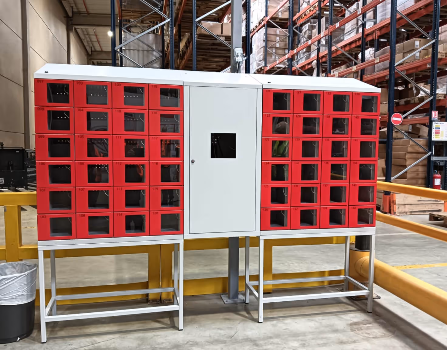 Red and white locker unit with multiple small compartments in a warehouse setting.