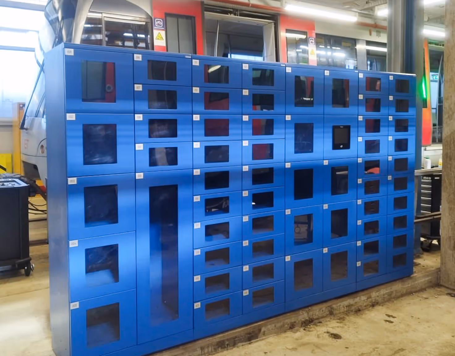Large blue locker system with multiple compartments in industrial setting near a train.
