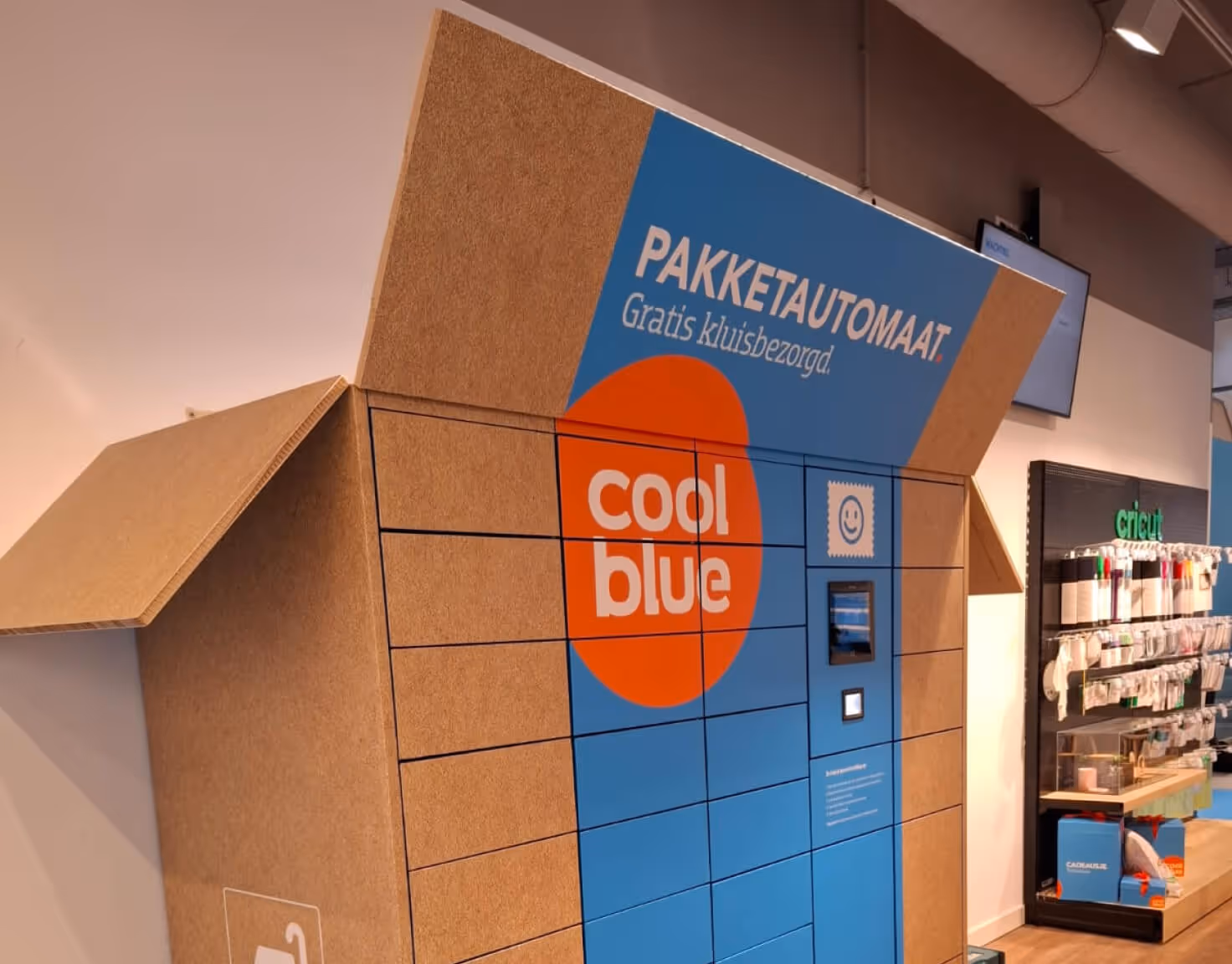 Package delivery locker resembling a cardboard house with Coolblue logo and touch screen interface.