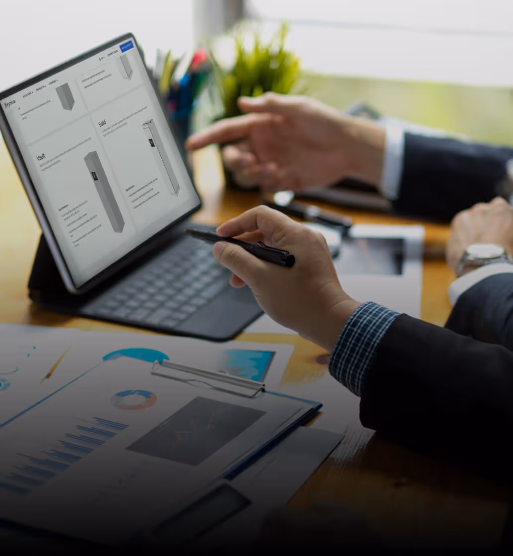 Two people in business attire discussing documents and product designs displayed on a tablet with a keyboard.