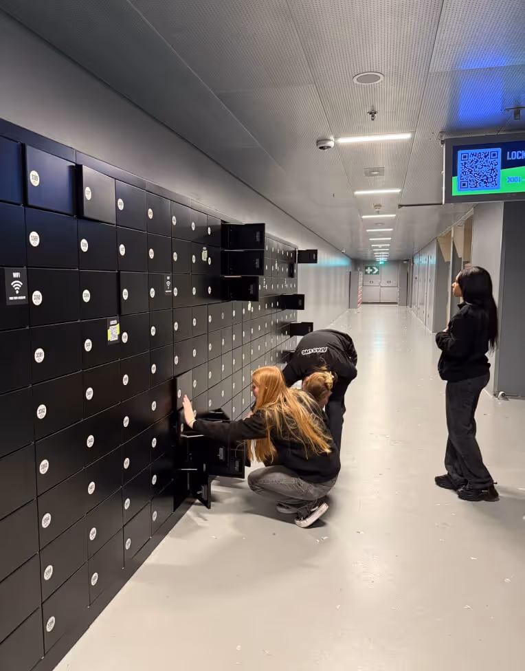 Three people interacting with black lockers in a long, well-lit hallway, two opening locker doors and one standing nearby.