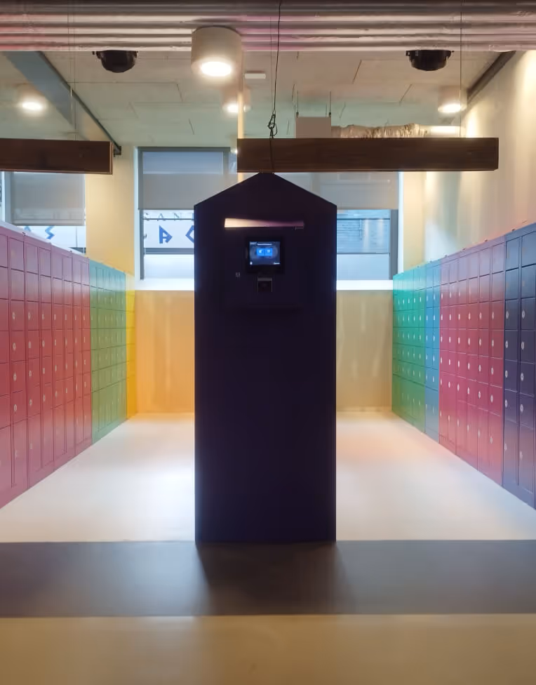 Room with colorful lockers on both sides and a tall dark kiosk with a screen in the center.