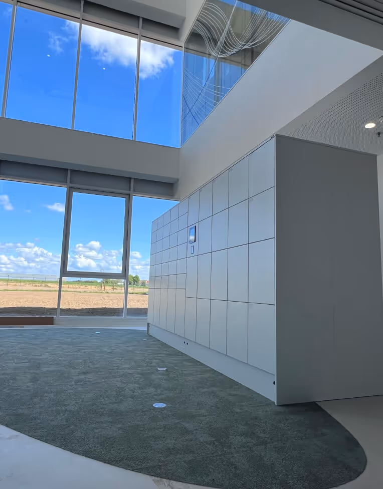 Modern interior with large windows showing a blue sky with clouds, a green carpeted floor, and a wall of white lockers.