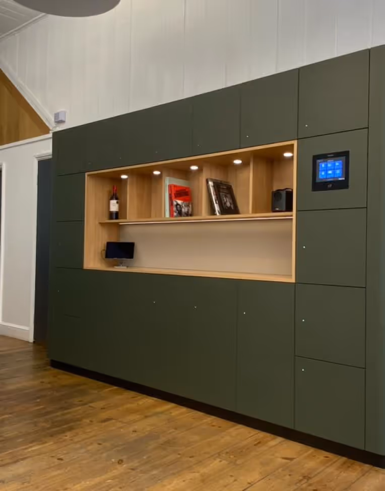 Modern green wall unit with wooden recessed shelves holding books, a bottle, a small speaker, and a digital touchscreen panel on the right.