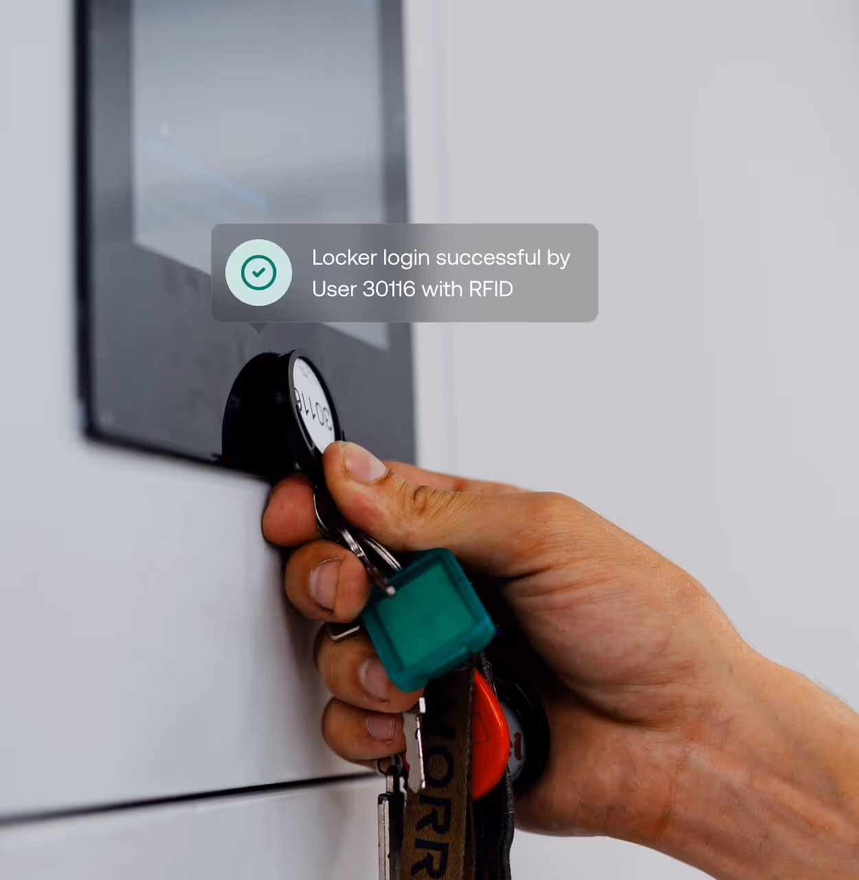 Hand holding RFID key fob to locker scanner with on-screen message confirming successful login by User 30116.