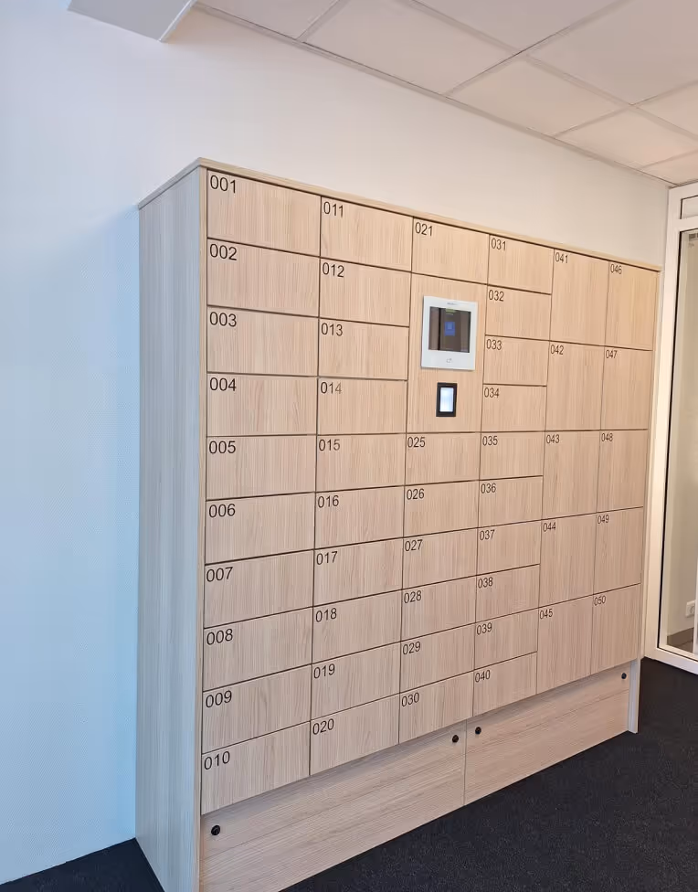Wall-mounted wooden parcel locker system with numbered compartments and a digital screen for access.