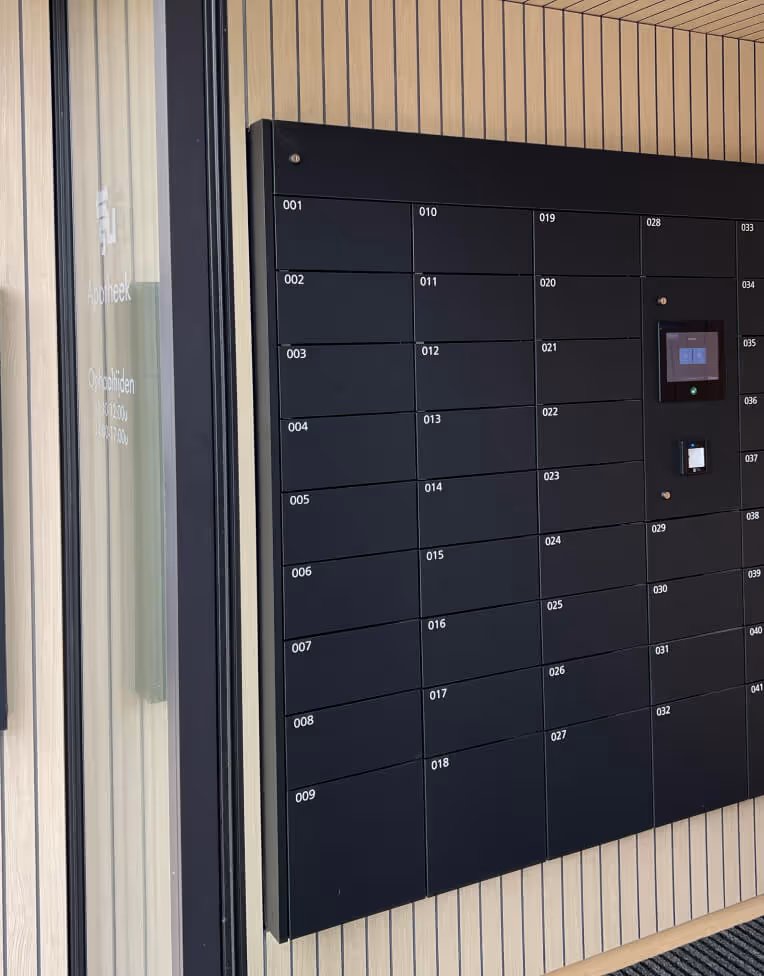 Wall-mounted black parcel locker with numbered compartments and digital access screens.