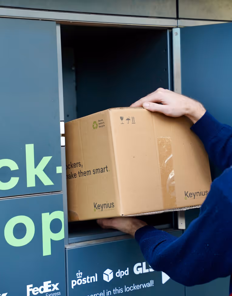 Person placing a cardboard box labeled Keynius into a parcel locker.
