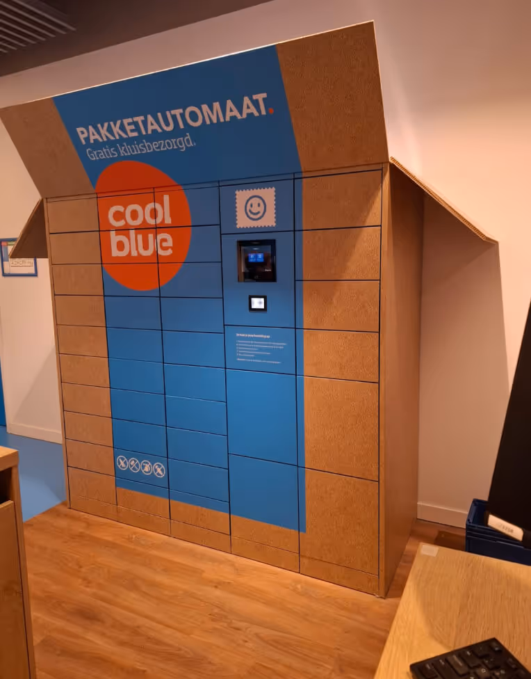 Indoor package locker system labeled Pakketautomaat with Coolblue logo, featuring multiple compartments and a digital screen for parcel pickup.