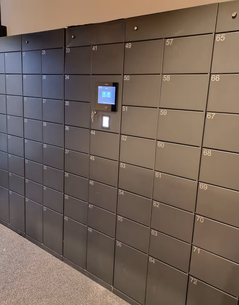Rows of numbered black parcel lockers with a digital touchscreen interface and key lock in the center section.