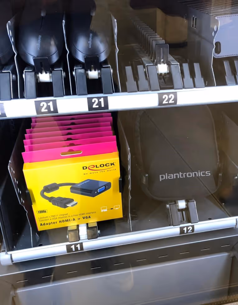 Vending machine shelves displaying two Logitech computer mice, a stack of Delock HDMI to VGA adapters in yellow packaging, and a Plantronics headset case.