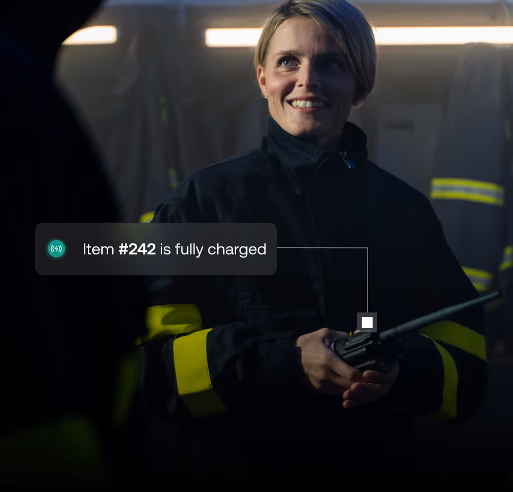 Smiling firefighter in uniform holding a handheld radio with a notification saying 'Item #242 is fully charged.'