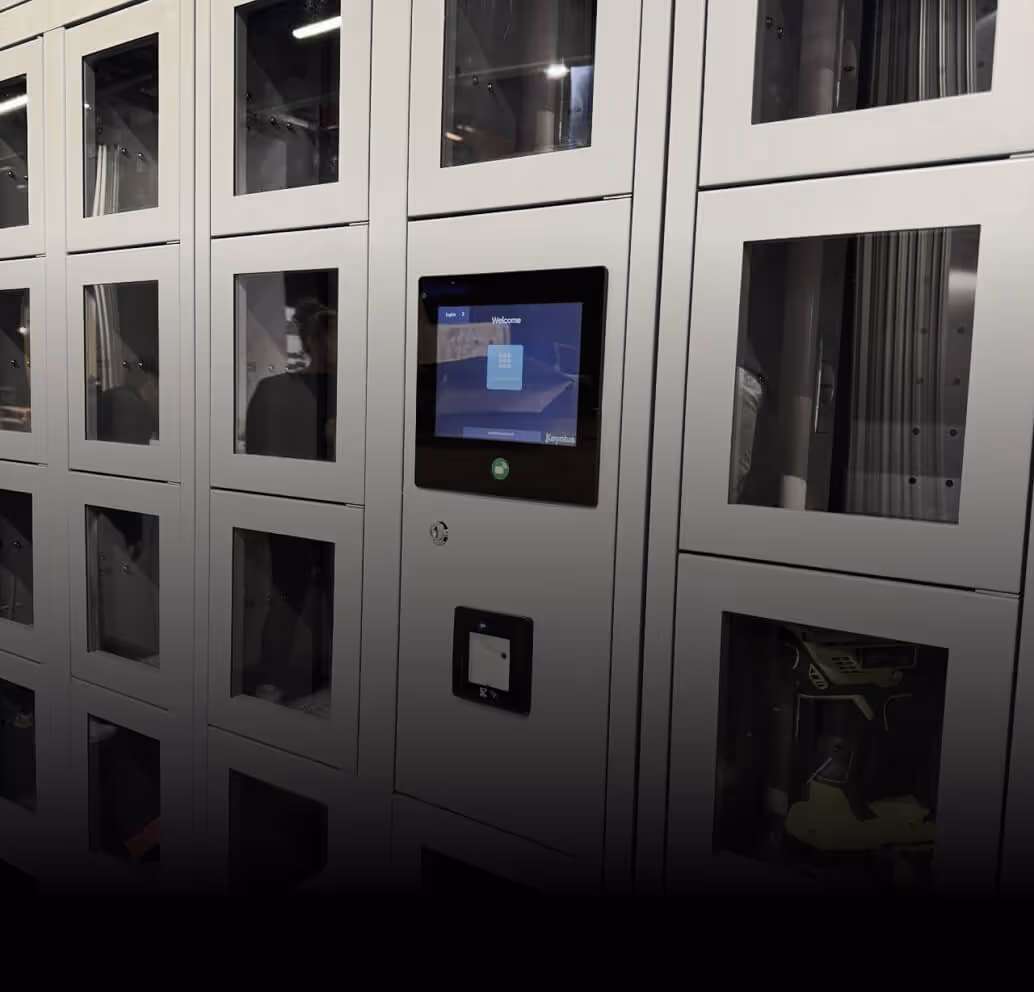 A wall of gray lockers with transparent windows and a central touchscreen interface for electronic access.