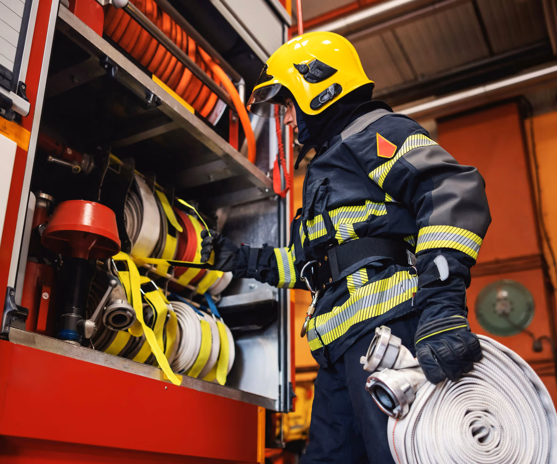 Firefighter in yellow helmet and protective gear handling fire hoses on a fire truck.