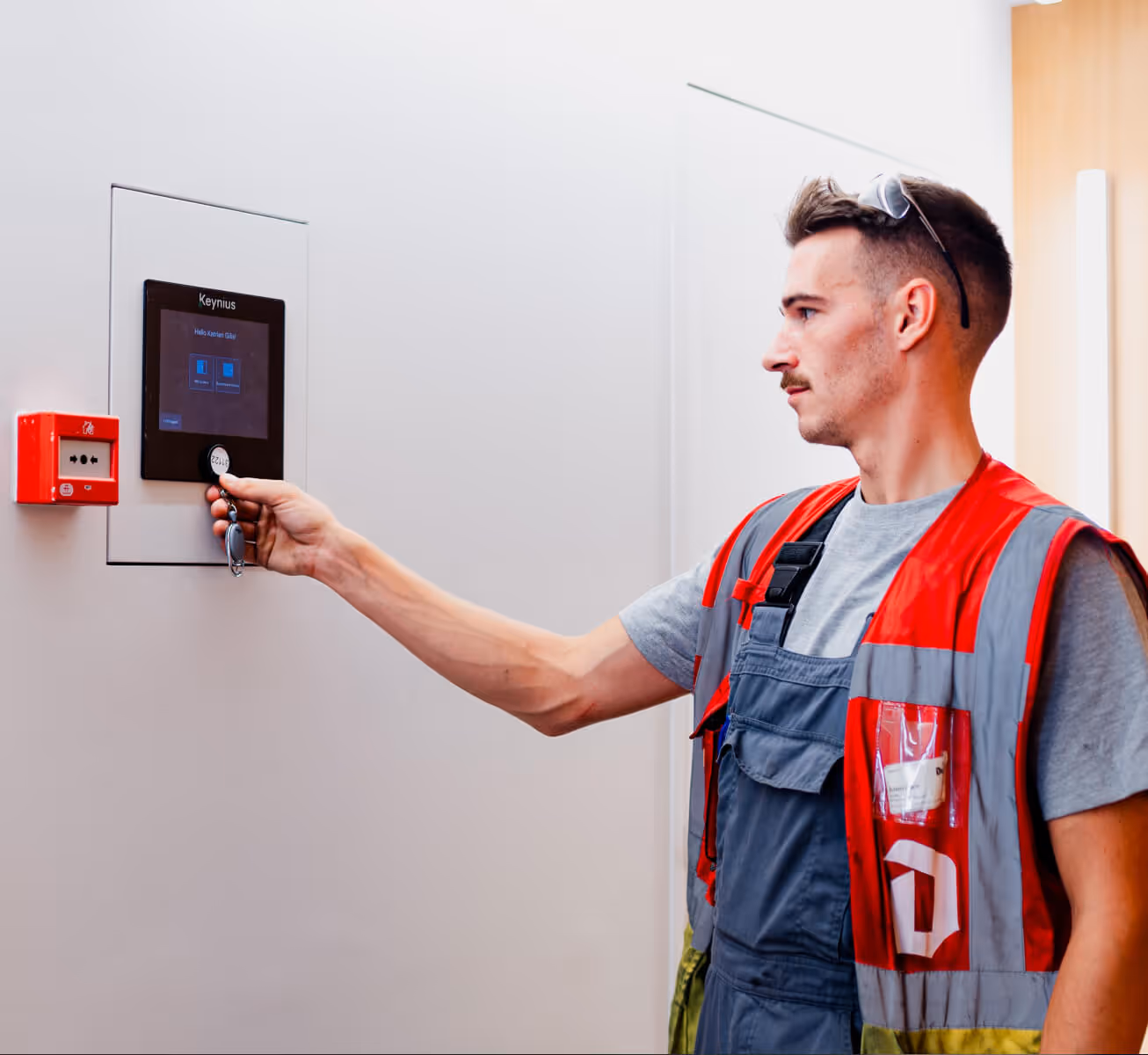 Worker in safety vest using a Keynius electronic key fob on a wall-mounted access control panel.