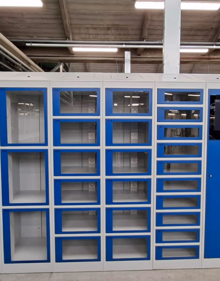 Empty modular storage lockers with blue-framed glass doors in an industrial warehouse setting.