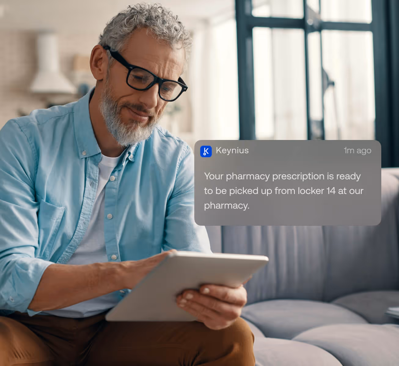 Older man with glasses sitting on a couch using a tablet, with a notification saying pharmacy prescription is ready for pickup from locker 14.